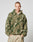 A person models the LIVE FAST DIE YOUNG Live Fast Teddy Jacket—a green and beige camo oversize fleece hoodie with zip-up front and visor hood—standing against a plain light gray background, hands in pockets.