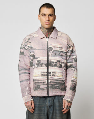 A man with short hair and tattoos stands facing forward, wearing the LIVE FAST DIE YOUNG LFDY Chase Jacket with a cars-in-traffic graphic print. He pairs it with loose jeans and poses against a plain white background.