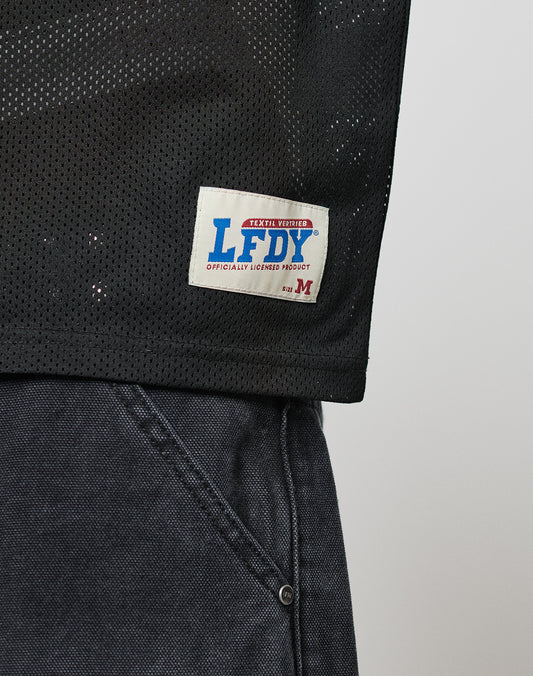 A close-up of the black mesh polyester LFDY Flash Jersey by LIVE FAST DIE YOUNG with a white label reading “LFDY Officially Licensed Product” in blue and red, shown next to dark gray denim pants.