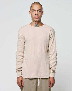 A person with a shaved head and neck tattoo stands facing forward, wearing the LIVE FAST DIE YOUNG Basic Regular Rib Longsleeve in beige and beige textured pants with white drawstrings, Regular Fit, against a plain light background.