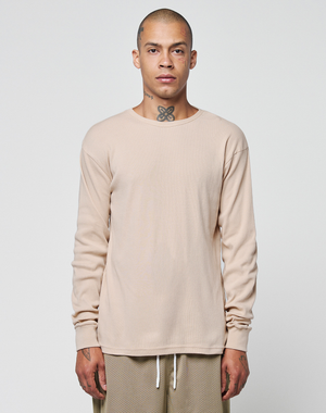 A person with a shaved head and visible neck tattoo stands facing forward, wearing the LIVE FAST DIE YOUNG Basic Regular Rib Longsleeve in beige and regular-fit light brown pants against a plain white background.