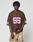 A person stands against a plain background wearing an oversize brown LIVE FAST DIE YOUNG LFDY Mesh Jersey with a V-neck and pink 55, paired with light tan camo-print polyester pants.