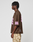 A person with short, twisted hair stands in profile wearing the LIVE FAST DIE YOUNG LFDY Mesh Jersey in brown with a pink 55 on the sleeve and back, styled oversized, paired with light camo pants against a plain light gray background.