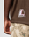 A close-up of a person wearing the LIVE FAST DIE YOUNG LFDY Mesh Jersey, an oversize brown mesh shirt with a pink and white L LIVEFAST patch, paired with camouflage pants. Their left arm hangs relaxed by their side.