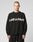A person with short hair models the LIVE FAST DIE YOUNG Live Fast Boucle Sweater—an oversize black polyester piece with LIVE FAST in bold white across the chest—against a plain light gray background.