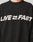 A person wears the Live Fast Boucle Sweater by LIVE FAST DIE YOUNG—an oversized black piece with LIVE FAST and a fast-forward arrow in bold white, crafted from soft Strick polyester for comfort and style.