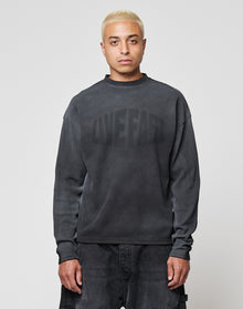 A person with short bleached blond hair wears the LIVE FAST DIE YOUNG LFDY Emblem Ghost Waffle Longsleeve, an oversized dark sweater with subtle lettering, and dark pants, standing facing forward against a plain light gray background. | model