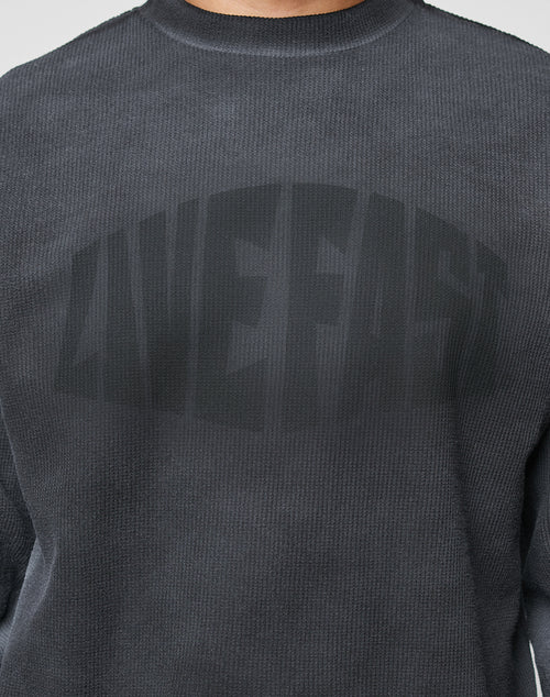 A close-up of the LFDY Emblem Ghost Waffle Longsleeve by LIVE FAST DIE YOUNG, a dark gray textured oversized sweatshirt with “LIVE FAST” in bold, arched black letters and a subtle sprayed effect across the chest.