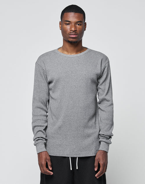 A man stands facing forward against a plain light gray background, wearing the LIVE FAST DIE YOUNG Basic Regular Rib Longsleeve in heather gray and black pants. He has a neutral expression with his arms at his sides.