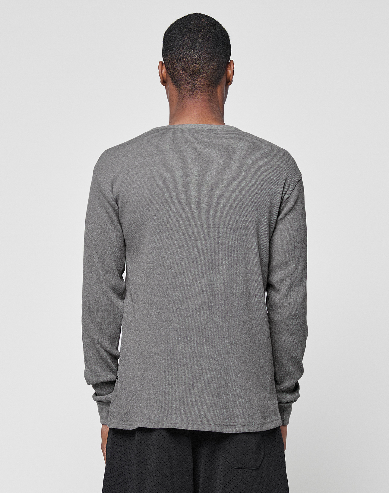 A person with short hair, facing away from the camera, wears the LIVE FAST DIE YOUNG Basic Regular Rib Longsleeve in gray and black cotton pants, set against a plain light gray background.