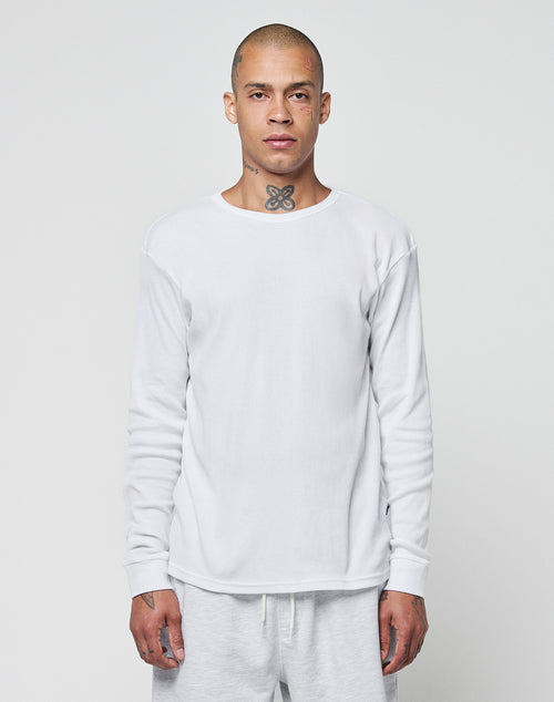 A person with a shaved head and neck tattoo wears the LIVE FAST DIE YOUNG Basic Regular Rib Longsleeve, a plain white shirt, along with matching white pants, standing against a light gray background and facing forward neutrally.