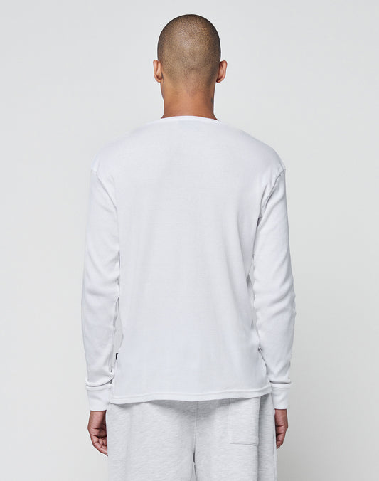 A person with a shaved head stands facing away from the camera, wearing the LIVE FAST DIE YOUNG Basic Regular Rib Longsleeve in white and light gray pants against a plain light background.