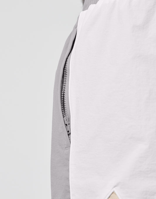 Close-up of LIVE FAST DIE YOUNG Basic Nylon Trackshorts in Regular Fit, showing a partially visible zipper between light gray and white Nylon-Lycra fabric, with a small beige triangle detail at the bottom edge.