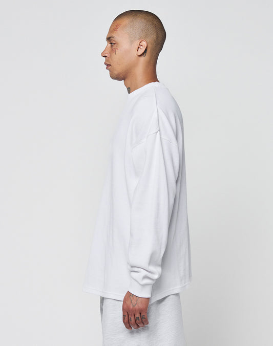 A person with a shaved head and tattoos, wearing an oversize fit white LIVE FAST DIE YOUNG Blank Waffle Longsleeve made of 100% Baumwolle with Ripp-Bündchen, stands in profile against a plain light background.