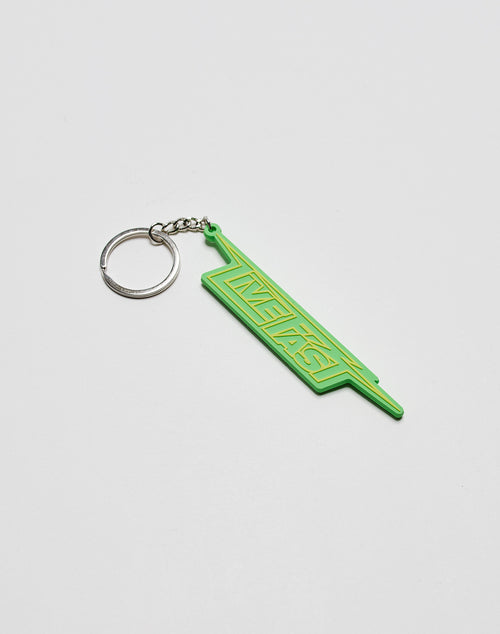 A green Live Fast Keychain by LIVE FAST DIE YOUNG, featuring INSTANT in yellow on silicone and attached to a metal ring, rests on a plain white surface.