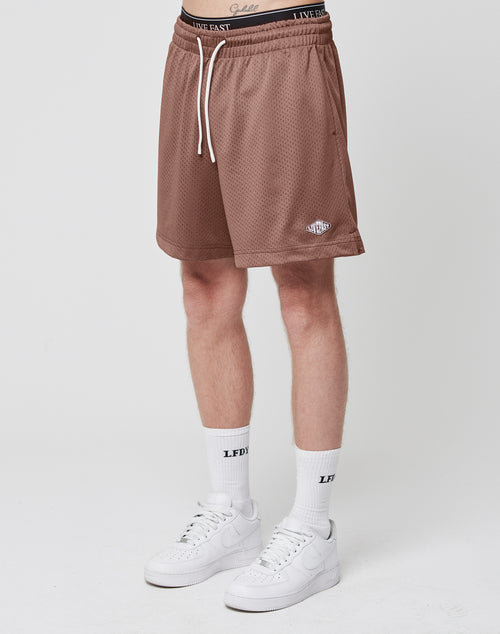 A person in LIVE FAST DIE YOUNG Basic Mesh Shorts with a logo patch and white drawstring, white socks with LFDY text, and white sneakers stands against a plain white background.