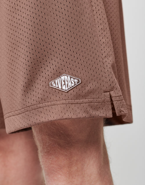 Close-up of a leg wearing LIVE FAST DIE YOUNG Basic Mesh Shorts in brown polyester, featuring a small logo patch with LIVEFAST near the hem.