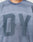 Close-up of a person wearing the LIVE FAST DIE YOUNG Faded Waffle Jersey, an oversized, textured blue shirt made from 100% Baumwolle with large blurred DY letters on the faded front; only neck and upper torso are shown.