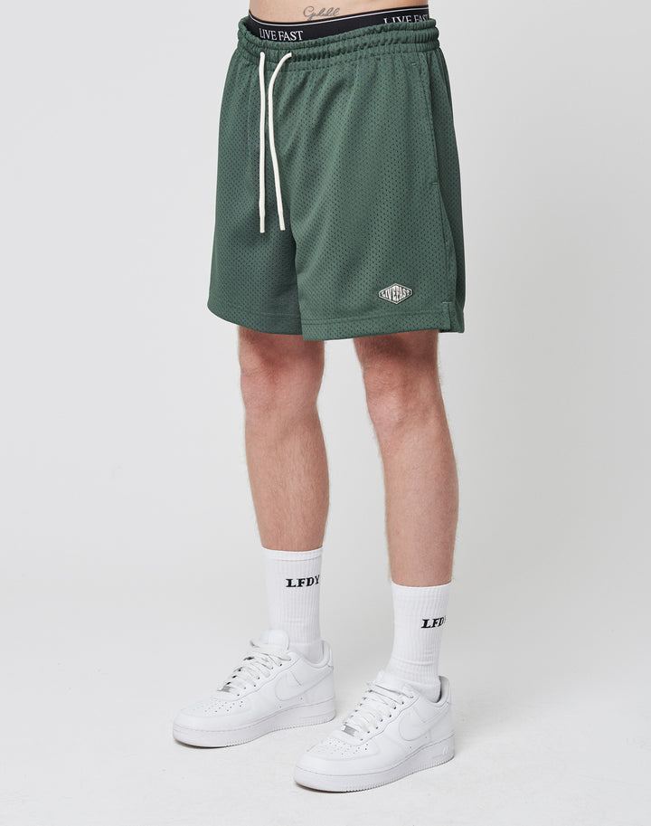 A person wearing LIVE FAST DIE YOUNG Basic Mesh Shorts in green, white crew LFDY socks, and white Nike sneakers stands against a plain white background. Only the lower body is visible.