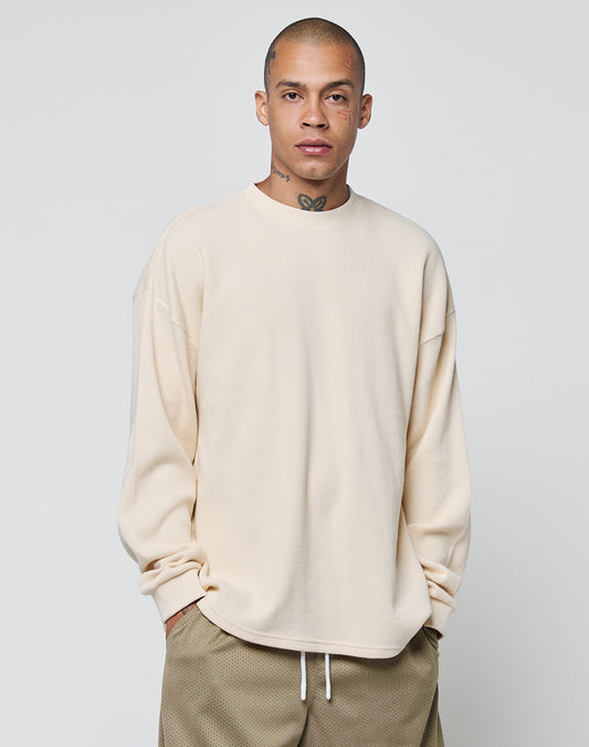 A person with closely shaved hair and face/neck tattoos wears the LIVE FAST DIE YOUNG Blank Waffle Longsleeve in light beige and brown drawstring shorts, standing against a plain light gray background.