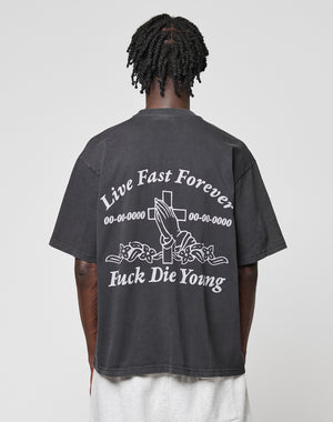 Seen from behind, a person with short, twisted hair wears the black LFDY Praying Tee by LIVE FAST DIE YOUNG, featuring white graphics of praying hands, a cross, roses, and the phrases Live Fast Forever and Fuck Die Young.