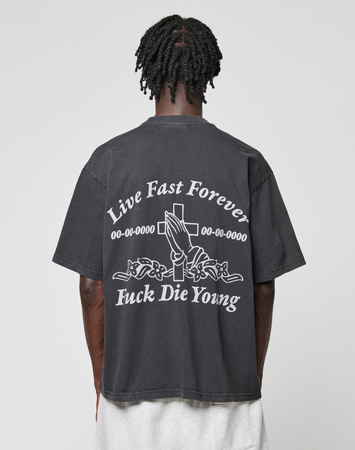 Seen from behind, a person with short, twisted hair wears the black LFDY Praying Tee by LIVE FAST DIE YOUNG, featuring white graphics of praying hands, a cross, roses, and the phrases Live Fast Forever and Fuck Die Young.