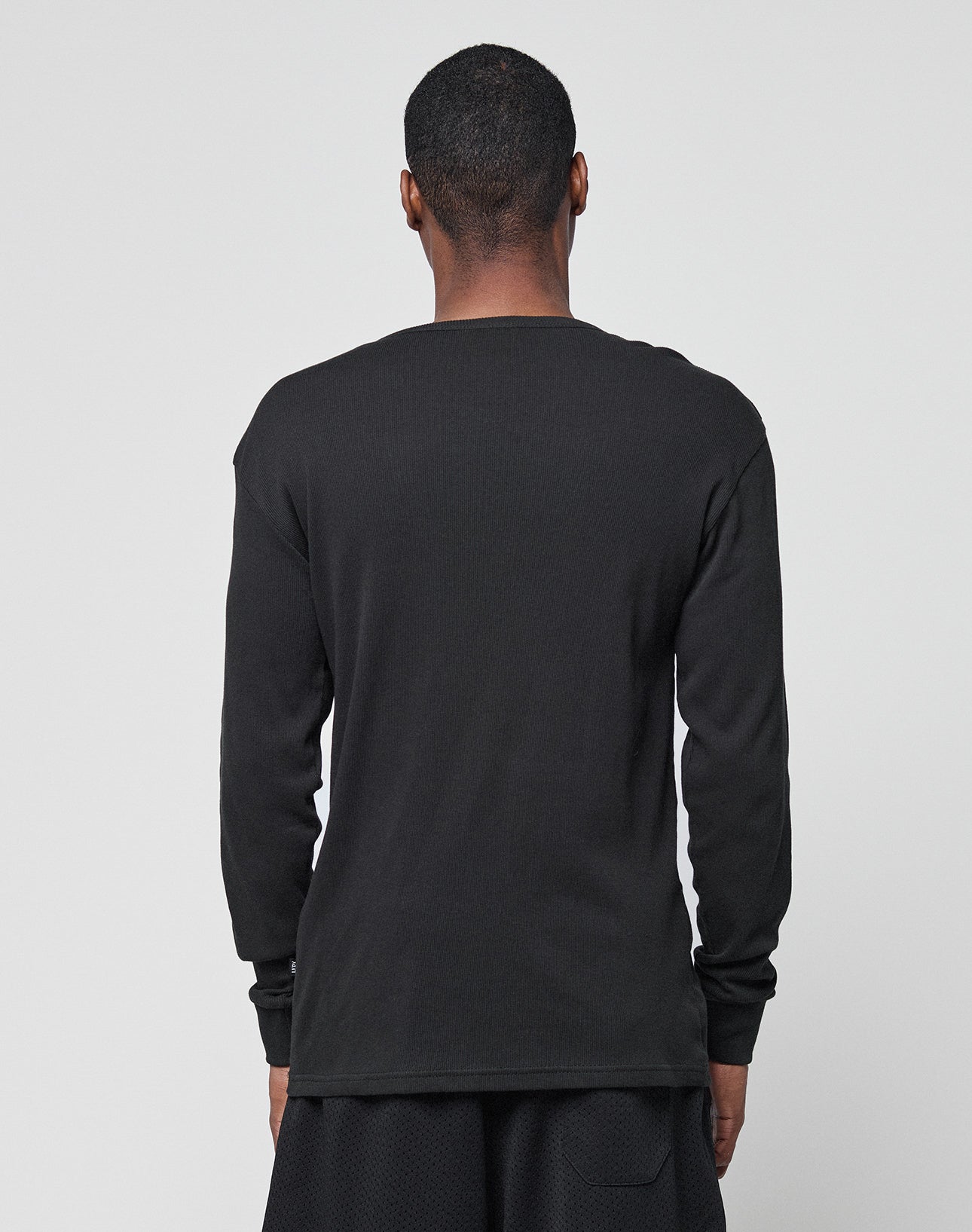 A person with short hair faces away from the camera, wearing the Basic Regular Rib Longsleeve by LIVE FAST DIE YOUNG and black polyester-cotton shorts against a plain light gray background.