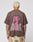 A person with short bleached blond hair is seen from behind, wearing the LFDY Flash Tee by LIVE FAST DIE YOUNG—an oversized brown cotton-slab shirt with a bold pink lightning bolt and LIVE FAST backprint—paired with tan camo shorts.
