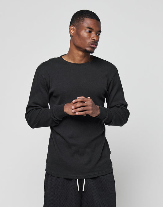 A man wearing the LIVE FAST DIE YOUNG Basic Regular Rib Longsleeve and black shorts in a regular fit stands against a light gray background with his hands clasped, looking slightly to the side.