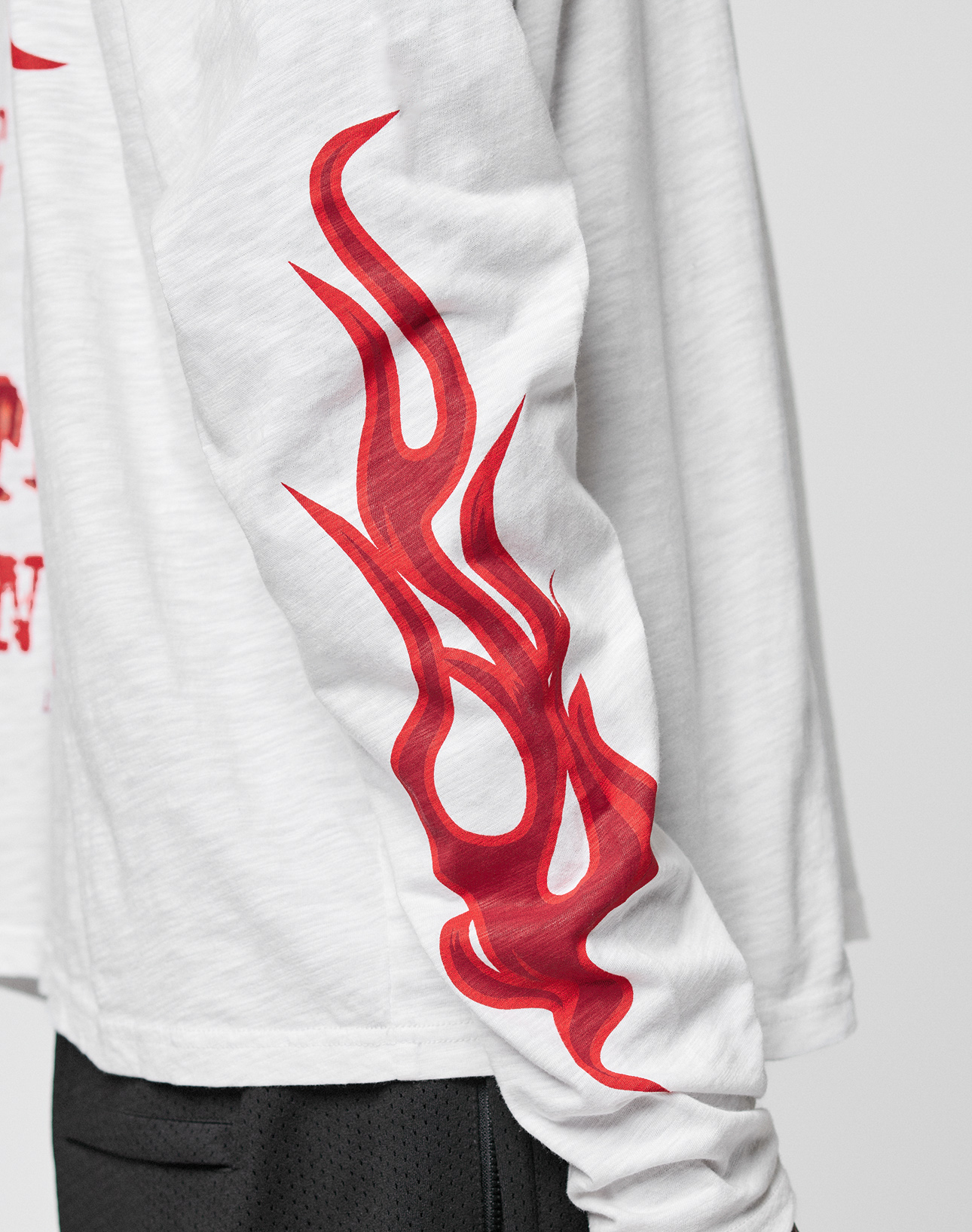 A person, shown from the side, wears the LIVE FAST DIE YOUNG LFDY We Walked Longsleeve in oversize fit with a bold red flame graphic on the sleeve, subtle logo frontprint, and black shorts.