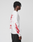 A person with short twisted hair stands sideways, wearing the LIVE FAST DIE YOUNG LFDY We Walked Longsleeve—an oversized white cotton shirt featuring red flame sleeve designs and a bold back logo print—paired with black pants.