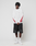 A person stands against a plain white background, wearing the LIVE FAST DIE YOUNG LFDY We Walked Longsleeve—an oversize white shirt with red flame sleeve designs and a subtle front logo—paired with black shorts, white socks, and white sneakers.