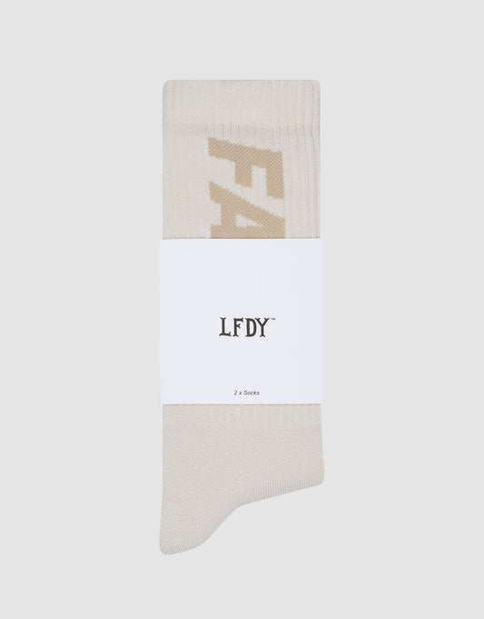 A single cream Basic Typo Sock from LIVE FAST DIE YOUNG is folded and wrapped with a white label reading "LFDY® 2x Socks" and care instructions, set against a plain light gray background.