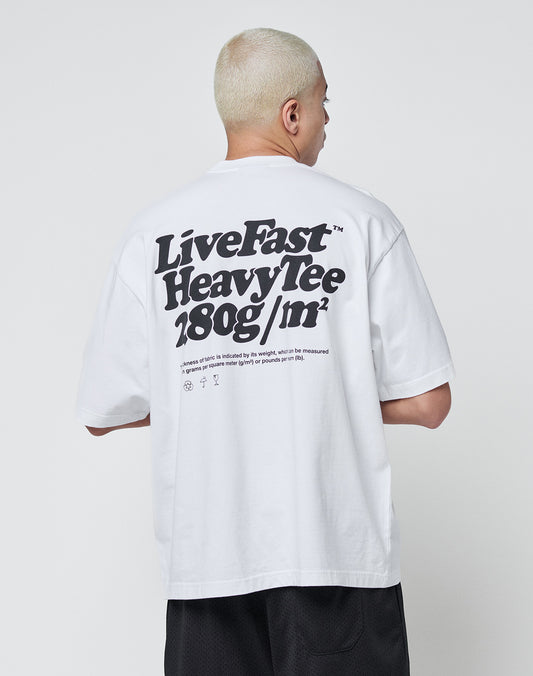 A person with short blond hair wears a white oversize Basic 280 Tee by LIVE FAST DIE YOUNG, featuring bold black backprint text and smaller text below, made from 100% cotton, standing against a plain white background.