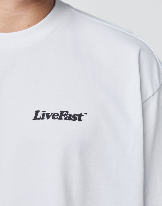 A person wearing the LIVE FAST DIE YOUNG Basic 280 Tee—an oversized, plain white 100% Baumwolle T-shirt with LiveFast in black on the left chest. Only their upper torso and part of their neck are visible.