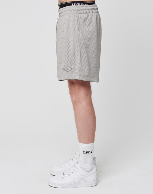 A person stands in profile against a plain white background wearing LIVE FAST DIE YOUNG Basic Mesh Shorts, white crew socks with LFDX text, and white Nike sneakers.