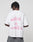 A person with short, twisted hair faces away from the camera, wearing the LFDY Against us Tee by LIVE FAST DIE YOUNG—an oversize white 100% Baumwolle t-shirt featuring a pink “WITH US OR AGAINST US” frontprint. The background is plain and light.
