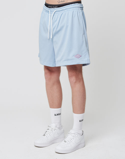 A person stands against a plain background wearing LIVE FAST DIE YOUNG Basic Mesh Shorts in light blue, white crew socks with black text, and white Nike sneakers. Only the lower half of the body is visible.