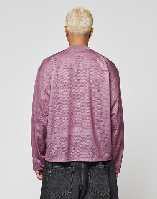 A person with short, bleached blonde hair is seen from behind wearing the LIVE FAST DIE YOUNG LFDY Flash Jersey—an oversize, long-sleeve mesh top in sheer lavender—with dark gray jeans against a plain light gray background.