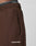 Close-up of a person wearing dark brown LFDY Pleated Jogger by LIVE FAST DIE YOUNG, featuring a side pocket and white LIVE FAST print near the pocket and on the elastic waistband. Plain light-colored background.