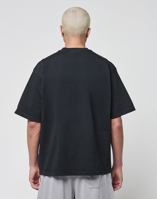 A person with short, bleached blond hair stands with their back to the camera, wearing a LIVE FAST DIE YOUNG Basic Tee in Oversize Fit and light gray mesh shorts against a plain light background.