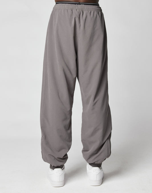 A person wears gray LFDY Trackpants by LIVE FAST DIE YOUNG, featuring an elastic waistband and cuffs, paired with white sneakers, standing against a plain light gray background.