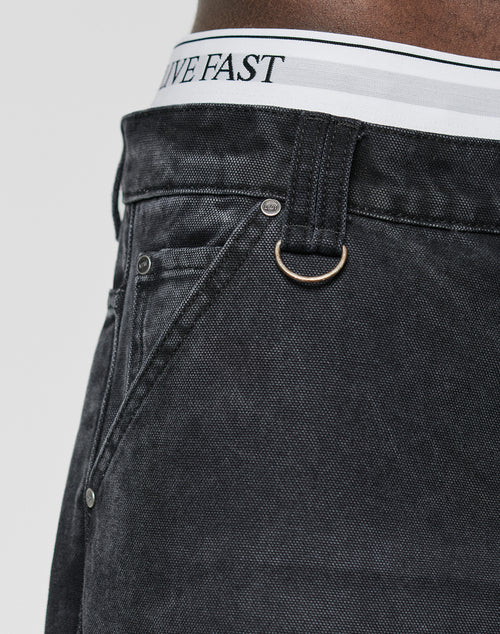 Close-up of a person wearing LFDY Carpenter Pants by LIVE FAST DIE YOUNG in a baggy fit, featuring a metal D-ring on the belt loop and a white waistband with LIVE FAST text visible above the jeans.