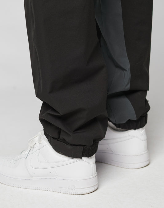Close-up of a person wearing LIVE FAST DIE YOUNG Basic Shell Pants with elastic waistband, drawstring, and elastic cuffs, paired with white Nike Air Force 1 sneakers. The inside lining of the oversize fit pants is visible.