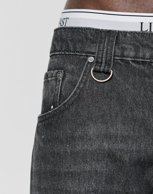 Close-up of a person wearing LFDY Baggy Denim jeans by LIVE FAST DIE YOUNG, featuring a metal ring on the belt loop and white underwear with black text peeking above the waistband, emphasizing the wide straight leg style.