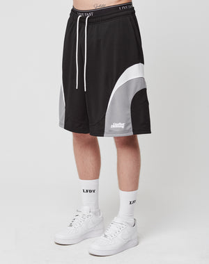 A person wears LIVE FAST DIE YOUNG Basic Trackshorts in black and white with an elastic waistband, paired with white LFDY socks and white Nike sneakers, standing against a plain white background.