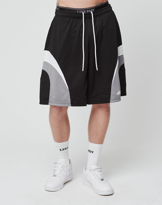 A person wears LIVE FAST DIE YOUNG Basic Trackshorts in black and gray with an elastic waistband and white drawstrings, LFDY logo-print white socks, and white sneakers. Only the lower half of the body is shown against a plain white background.