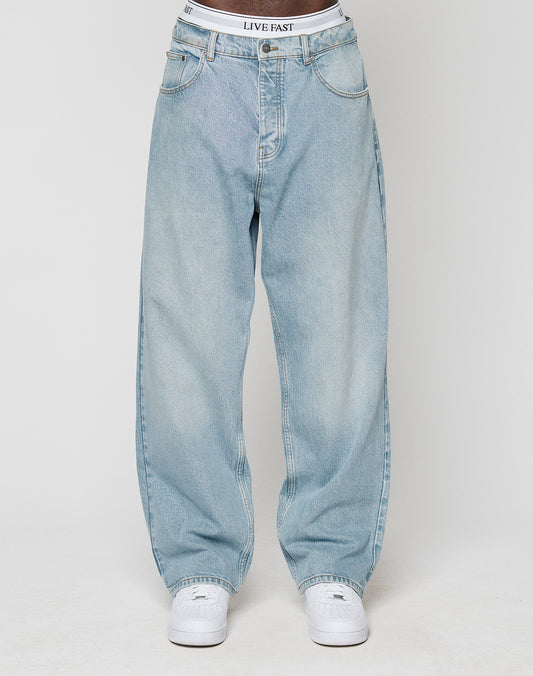 A person wearing light blue LFDY Baggy Denim by LIVE FAST DIE YOUNG, white sneakers, and a visible white waistband with LIVE FAST text, stands against a plain light background.