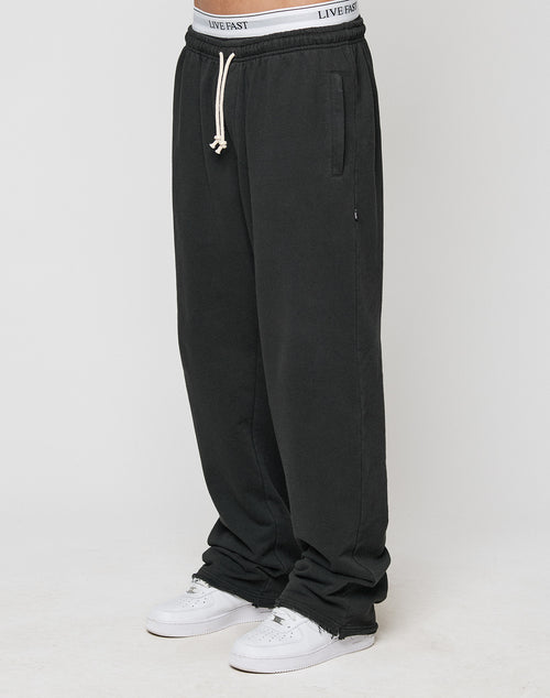 A person in LIVE FAST DIE YOUNG LFDY Lightweight Joggers with elastic waistband and drawstring, paired with white sneakers and a visible white LIVE FAST waistband, stands against a simple light background.