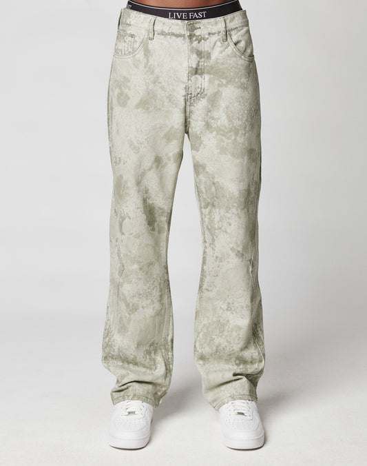 A person models the Rhomb Wide Denim by LIVE FAST DIE YOUNG—light gray acid-wash, baggy jeans with a black LIVE FAST waistband—paired with white sneakers, all set against a plain white background.